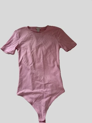 Rosa kortärmad body - Säljer en enkel och stilren rosa bodysuit med korta är, rund hals och mjukt bomullsmaterial. Perfekt att styla med jeans eller kjol för en clean look.