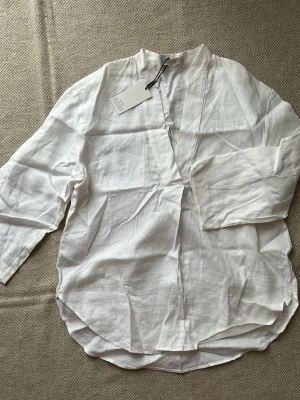 Mng Vit linneskjorta från Mango med v-ringning - Säljer en stilren vit skjorta från Mango i luftigt linne. Skjortan har v-ringad hals, trekvartsärm och avslappnad passform. Perfekt för dig som gillar minimalistisk och clean stil. Lappen sitter kvar.