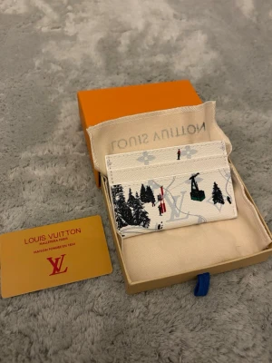 Snygg vit korthållare  - Snygg vit korthållare med vinterinspirerat tryck av granar, skidåkare och liftar. Tillverkad i tåligt canvasmaterial med klassisk logga i bakgrunden. Kommer med original ask och dustbag. Perfekt för dig som vill ha något unikt och trendigt.