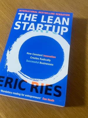 The Lean Startup av Eric Ries - En blå pocketbok med titeln 'The Lean Startup' av Eric Ries. Omslaget har en vit cirkel och text i vitt, blått och orange. Boken handlar om innovation och hur man bygger framgångsrika företag. Perfekt för dig som är intresserad av entreprenörskap och affärsutveckling.