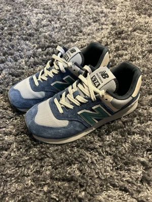 New Balance 574  - Snygga New Balance 574 sneakers i blått och grått med turkosa detaljer. Ovandelen är i mocka och mesh, med klassisk N-logga på sidan och vita snören. Skön och tidlös modell som passar till många stilar.