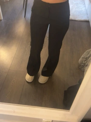 Svarta kostymbyxor med rak passform - Snygga svarta kostymbyxor med hög midja och rak passform. Byxorna har klassisk design med diskret knapp och dragkedja framtill. Perfekta för en stilren look och lätta att matcha med olika toppar.