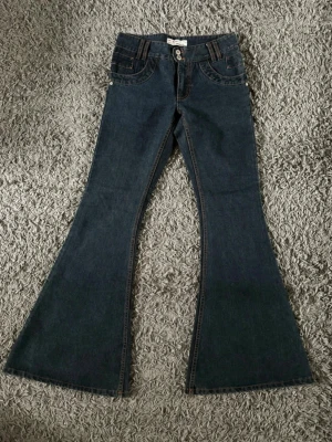 Mörkblå utsvängda jeans från ICHI - Säljer ett par mörkblå jeans från ICHI med riktigt snygg utsvängd passform. Jeansen har dubbla knappar i midjan, dekorativa sömmar och klassiska fickor fram. Perfekta för dig som gillar retrostil och vill sticka ut lite extra.