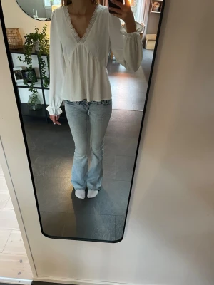 Vit blus med spetsdetaljer - Vit blus med v-ringning och fina spetsdetaljer från Vero Moda. Blusen har långa, lätt puffiga ärmar med resår vid ärmslut och ett avslappnat fall. 