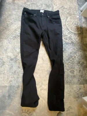 Svarta bootcut jeans från 107 - Säljer ett par svarta bootcut jeans från 107. Jeansen har klassisk femficksdesign, normal midja och utsvängda ben. Materialet är kraftigt denim i bomull. Perfekta för dig som gillar en tidlös och enkel stil.