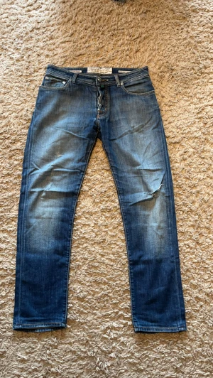 Blå jeans från Jacob Cohen - Snygga blå jeans från Jacob Cohen med klassisk femficksmodell och raka ben. Jeansen har slitningar och tvättade detaljer för en cool, avslappnad look. Tillverkade i mjukt denimtyg med kontrastsömmar och patch med logga bak i midjan. Storlek 33 sjukt snygg färg 