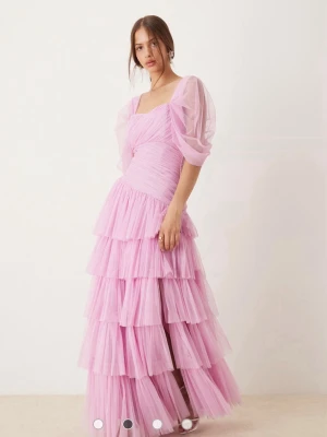 Lång rosa volangklänning med puffärm - Långklänning i ljusrosa med flera lager volanger och puffärmar. Klänningen har en v-ringad front, transparenta ärmar och dragkedja i ryggen. Materialet är lätt och troligtvis polyester eller syntet, perfekt för speciella tillfällen. Perfekt till bal🩷