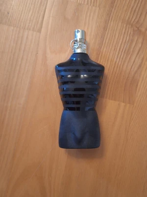 Jean Paul Gaultier Le Male parfym - Säljer en Jean Paul Gaultier Le Male parfym i den ikoniska flaskan formad som en manlig torso. Flaskan är mörkblå med svarta ränder och har ett silverfärgat sprayhuvud. Parfymen kommer med en rund röd sammetsbas med guldkant. Helt oandvänd fast utan prislapp. 