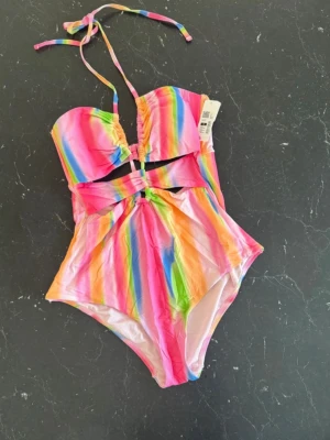 Fin baddräkt i strl M - Säljer en färgglad baddräkt från Cubus. Ny med prislapp på. Modellen har cut out-detaljer framtill, bandeauformad överdel och smala axelband som knyts i nacken. Storlek M