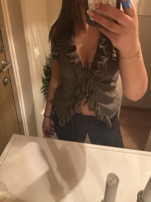 Brun croppad blus med volanger - Säljer en brun croppad blus med volangdetaljer och knyt framtill. Toppen har djup v-ringning och korta ärmar. Perfekt för dig som gillar trendiga detaljer och en feminin look.