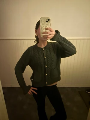 Grå  kabelstickad kofta - Mysig grå  kabelstickad kofta med rund hals och guldfärgade knappar. Koftan har två stora fickor framtill och ribbade muddar vid ärmslut och nederkant. Perfekt för lager-på-lager och en chill look. Aldrig använd. Köpt vanligtvis för 600