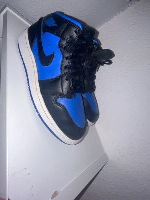 Air Jordan 1 mid Royal blå/svart - Säljer ett par Air Jordan 1 Retro High i färgerna royal blå och svart. Skorna har klassisk hög siluett, svart swoosh och blå detaljer på tå, häl och krage. Ovandelen är i läder och sulan är vit med blå yttersula. Perfekta för dig som gillar ikoniska sneakers. Skriv för frågor eller om mer bilder, skorna är 100% äkta