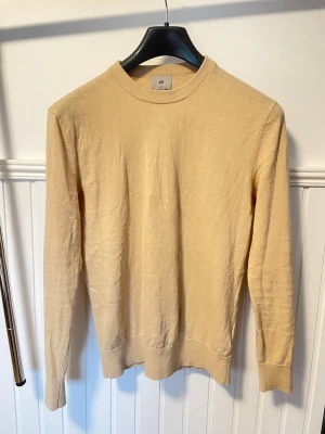 Gulbeige stickad tröja från H&M (bomull- cashmire) - En stilren gul/beige tröja från H&M med rund halsringning och långa ärmar. Tillverkad i ett mjukt och tunt bomull & cashmire material som passar perfekt för alla tillfällen. Pris kan diskuteras vid snabb affär.
