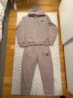 Brun Nike tracksuit  - Säljer ett set beige mjukisbyxor och hoodie från Nike med broderad svart logga på vänster ben och bröst. Byxorna har resår i midjan och vid bensluten samt sidofickor. Perfekta för en avslappnad och chill stil.