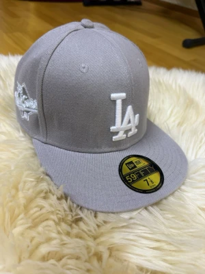New Era keps  - Snygg grå 59FIFTY keps från New Era med LA Dodgers-logga broderad i vitt framtill och mästerskapsmärke på sidan. Klassisk flat brim och strukturerad passform. Tillverkad i bomullsmix, perfekt för_riktigt clean streetstyle. DEN ÄR TYP SOM NY, HAR KNAPPT ANVÄNT DEN!!