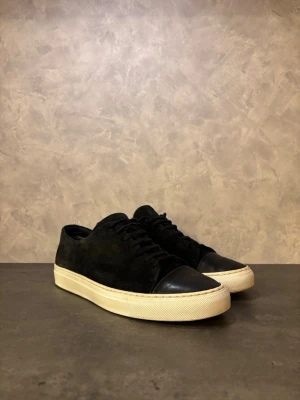 Axel Arigato Clean 90s - Stilrena svarta Axel Arigato Clean 90 med ovandel i mocka och tåparti i slätt läder. Skorna har en vit, klassisk gummisula och diskret design. Perfekta för en clean och modern look. I bra skick!