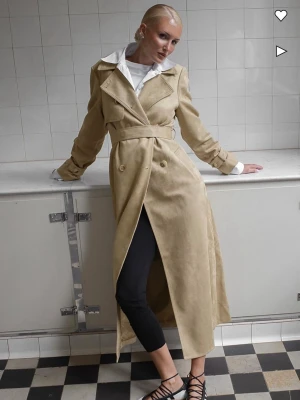 Beige lång trenchcoat med bälte - Säljer denna fina nästan slutsålda beigea kappan ifrån Lovisa Worges kollektion med NAKD. Använd få tal gånger så är i väldigt bra skick! Köpt för 1399