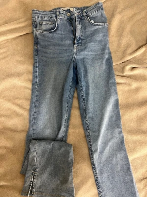 Ljusblå raka jeans med slits - Säljer ett par ljusblå jeans med raka ben och snygg slits vid benslutet. Klassisk femficksmodell med dragkedja och knapp. Jeansen har en avslappnad passform och är tillverkade i mjuk denim. Perfekta till sneakers eller boots för en cool vardagslook. Skicka gärna prisförslag