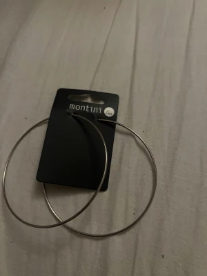 Stora silvriga hoops från Montini - Säljer ett par stora, tunna hoops i silverfärgad metall från Montini. Klassisk rund form som ger en clean och trendig look. Perfekta för dig som gillar statementörhängen och vill addera lite edge till din stil.