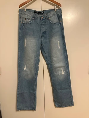 Ljusblå raka jeans från Rocawear - Säljer ett par ljusblå jeans från Rocawear med raka ben och slitna detaljer framtill. Jeansen har klassisk femficksmodell och coola broderade loggor på bakfickorna. Tillverkade i denim med en avslappnad passform. Lägger sig snyggt över skorna.