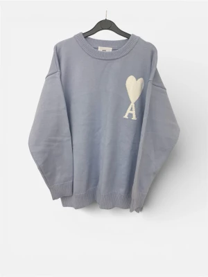 Ljusblå stickad Ami Paris tröja - Ljusblå oversized stickad tröja med rund halsringning och ribbade muddar. På bröstet finns en vit hjärtdetalj och bokstaven A. Perfekt för dig som gillar en enkel men ändå unik look.
