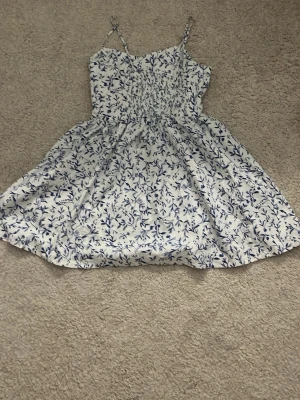 Vit och blå blommig sommarklänning - Söt kortklänning med smala axelband och blått blommönster och jättestretchig midja, andvänd fåtal gånger!