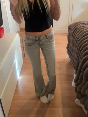 Gråa bootcut jeans med fickor - Säljer ett par gråa bootcut jeans med klassiska fem fickor och snygga sömmar. Jeansen har en låg midja och silverfärgade knappar samt detaljer på bakfickorna. Perfekta för en avslappnad och trendig look.