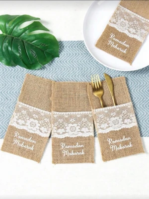 Bestickfickor Ramadan - Säljer dekorativa bestickfickor i jute med vit spets och texten 'Ramadan Mubarak' framtill. Perfekta för att duka fint under Ramadan. Fickorna är bruna med vit spetsdetalj och har plats för kniv, gaffel och sked. Det är 5 stycken 
