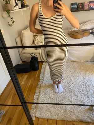 Randig långklänning i bomull - Snygg långklänning med svarta och vita ränder. Klänningen är ärmlös med rundad halsringning och har en tight passform som framhäver figuren. Perfekt för en avslappnad och trendig look.