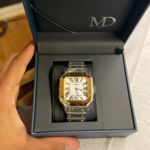 Seiko klocka i guld och silver - Stilren Seiko klocka med fyrkantig urtavla i vitt och romerska siffror. Boetten är guldtonad och armbandet är i silver med gulddetaljer. Klassisk design som passar till många stilar med NH32 movement, alltså inget batteri.