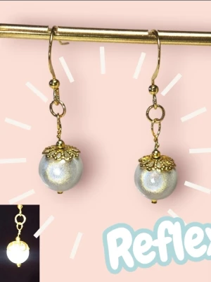 Guldiga reflex örhängen med pärlor - Snygga örhängen med guldpläterade krokar och skimrande vita pärlor. Örhängena har dekorativa guldfärgade detaljer ovanför pärlan som ger en elegant touch. Perfekta för att lyfta vilken outfit som helst med lite extra bling. Stark reflex i akrylpärlorna, syns väldigt bra i trafiken eller om du blir fotad med blixt.