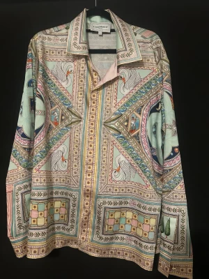 Mönstrad silkesskjorta från Casablanca - Unik långärmad skjorta från Casablanca i silke med detaljerat och färgstarkt mönster i pastellfärger, inslag av vitt, grönt, rosa och blått. Skjortan har klassisk krage, knappar framtill och exklusiv känsla. Perfekt för dig som vill sticka ut.