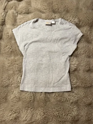 Ljusgrå topp från Gina Tricot - En enkel och stilren ljusgrå topp från Gina Tricot. Toppen har rund halsringning och korta ärmar. Perfekt basic T-shirt. 