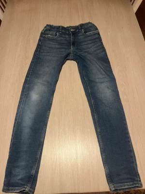 Blå slim fit jeans med slitningar - Snygga blå slim fit jeans med lätt slitna detaljer och klassisk femficksdesign. Jeansen har normalhög midja, knappgylf och raka ben. Materialet är troligtvis bomull med lite stretch för extra komfort. Perfekta till en avslappnad stil.