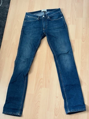 Acne Studios Mörkblå Jeans - Säljer ett par klassiska mörkblå jeans från Acne Studios med raka ben och fem fickor. Jeansen har snygga slitningar och kontrastsömmar. Perfekta till en avslappnad stil och tillverkade i slitstark denim.