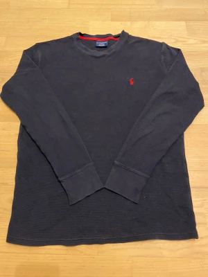 Marinblå långärmad tröja Polo Ralph Lauren - Klassisk marinblå långärmad tröja från Polo Ralph Lauren med röd broderad logga på bröstet. Tröjan har rund halsringning.