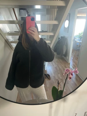 Mörkgrå teddyjacka med dragkedja - Säljer en fluffig mörkgrå teddyjacka med hög krage och dragkedja framtill. Jackan har en avslappnad passform och är perfekt för att hålla värmen. Materialet är mjukt och gosigt, vilket gör den superbekväm att bära.