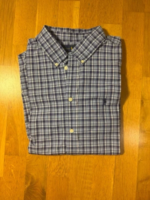 Blårutig skjorta från Ralph Lauren - Storlek S = 18-20. Klassisk blårutig skjorta från Ralph Lauren med button-down krage och vita knappar. Skjortan har lång ärm och är tillverkad i mjuk bomull. Perfekt för en avslappnad men ändå stilren look.