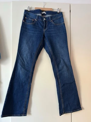 Blå bootcut jeans med fickor - Snygga blå bootcut jeans med klassiska fem fickor och kontrastsömmar. Jeansen har normalhög midja och vida ben som ger en retrovibe. Tillverkade i denim med en djupblå tvätt och detaljer i silverfärg. Perfekta för dig som gillar en avslappnad men trendig stil.