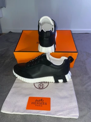 H sneakers  - Snygga svarta sneakers med chunky, räfflad vit sula och svarta skosnören. Skorna har en låg profil och är tillverkade i läder med vita detaljer på insidan. Perfekta för dig som vill ha en exklusiv och modern look.