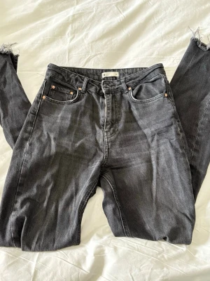 Svarta straight leg jeans från Gina Tricot - Säljer ett par svarta straight leg jeans från Gina Tricot, modell perfect jeans. Jeansen har hög midja, klassiska fem fickor och råa, fransiga benslut för en trendig look. Materialet är kraftig denim i bomull. Perfekta till en avslappnad stil!