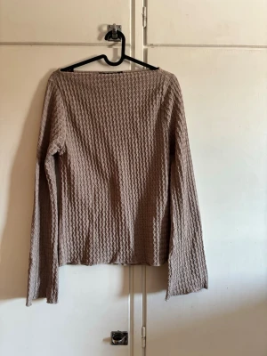 Beige långärmad topp med struktur - Säljer en beige långärmad topp med våfflad struktur och rak passform. Tröjan har bred halsringning och är tillverkad i ett mjukt, stretchigt material som känns skönt mot huden. 
