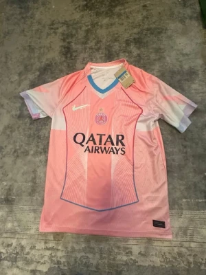 PSG rosa matchtröja från Nike - Snygg rosa PSG matchtröja från Nike med vita och blå detaljer. Tröjan har klubbmärke och Qatar Airways-logga på bröstet samt vit Nike-swoosh. Tillverkad i lätt och ventilerande material, perfekt för fotboll eller träning.