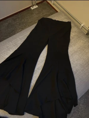 Svarta vida bootcut byxor - Säljer ett par svarta byxor med riktigt vida ben och bootcut-modell. Byxorna har hög midja och är sydda i ett mjukt, stretchigt material som ger en snygg siluett. Perfekta för dig som vill sticka ut med en trendig look.