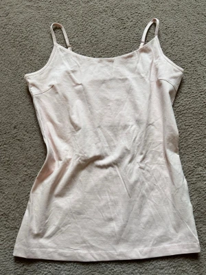 Klassisk simpel ljusrosa linne - Säljer en ljusrosa linnetopp med smala axelband och rak passform. Toppen är ärmlös och gjord i mjuk bomull, perfekt för varma dagar eller som lager under andra plagg! Den har justerbara axelband och extra tyg vid brösten, så inget syns igenom😻Enkel och stilren design utan mönster eller detaljer. Storlek M! Aldrig använd men bortklippt lapp❣️