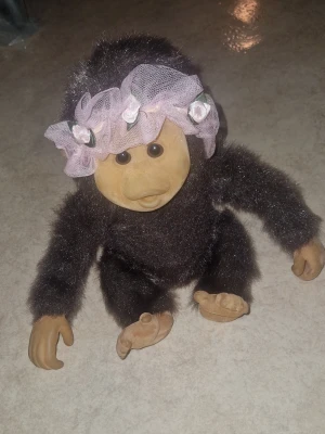 Gosse djur Little Monkey Lost - Söt mjuk apa. Apan har ett rosa diadem med tygblommor och nät, vilket ger den ett gulligt utseende. Perfekt som prydnad eller leksak. Inga defekter.