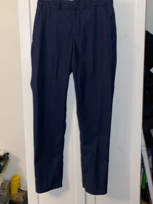 Mörkblå kostymbyxor med raka ben - Snygga mörkblå kostymbyxor med klassisk rak passform och hällor för skärp. Byxorna har diskreta fickor och är perfekta för en stilren look. Materialet känns mjukt och har en lätt glans, vilket ger en dressad känsla.