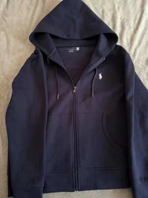 Marinblå hoodie från Polo Ralph Lauren - Ralph Lauren zip up i storlek S. Säljer den eftersom att jag inte alls tar på mig den. Jag vill helst bli av med den. Pris kan diskuteras vid snabb affär. Möts upp i gbg!.