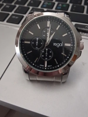 Regal herrklocka i rostfritt stål - Stilren herrklocka från Regal med svart urtavla och silverfärgade detaljer. Klockan har tre mindre urtavlor, tydliga markeringar och ett klassiskt armband i rostfritt stål. Perfekt accessoar för dig som gillar en tidlös look.