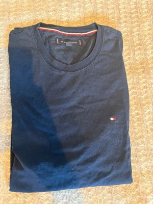 Mörkblå t-shirt Tommy Hilfiger - Säljer en mörkblå t-shirt från Tommy Hilfiger. Materialet är bomull och storleken är M. Tröjan är i bra skick och har inga synliga defekter.
